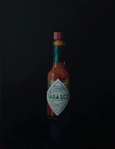 A bottle of Tabasco hot sauce against a dark background.