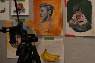 Art sketches taped on a wall with a lamp and tripod in the foreground.