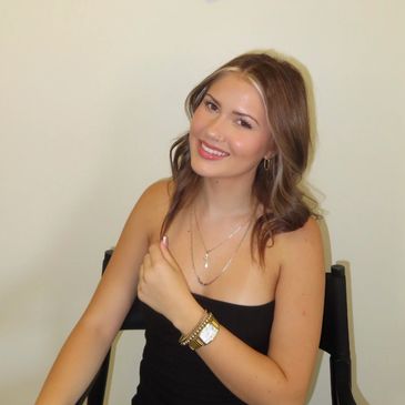 Young woman smiling while sitting on a chair against a plain background.