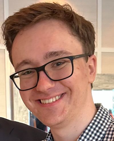 Young man with glasses smiling warmly at the camera.