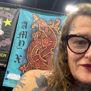 Close-up of a woman with a tattoo and glasses at an AMVX booth.