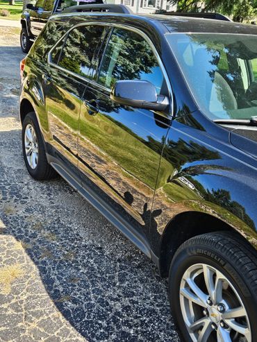 Shiny black SUV reflecting trees and sky on its surface.