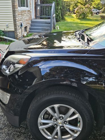 Close-up of a black Chevrolet car front wheel and fender near a house.