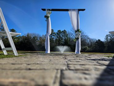 Outdoor wedding arch with white drapes and flowers on sunny day.