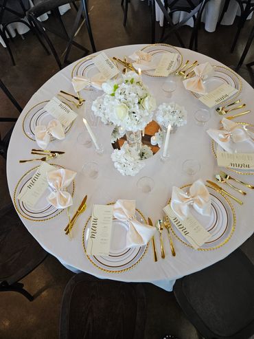 Elegant round table setup with white floral centerpiece and gold cutlery.