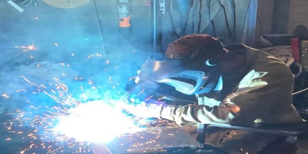 Person welding metal with sparks and bright light in a fabrication & welding shop.