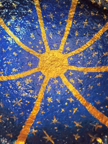 Closeup of papier mache bowl that is painted with a gold sun and stars over a blue night sky.
