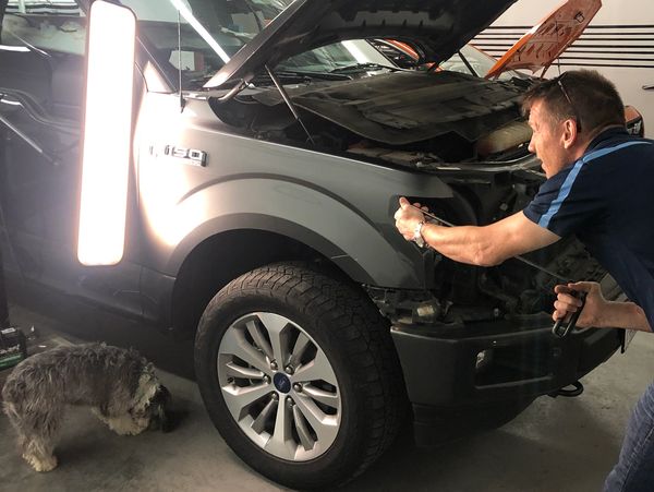 A man is fixing hail damage on a grey car.