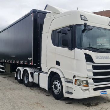 White Scania semi-truck with a black trailer parked on a concrete surface.