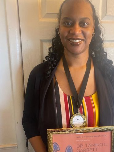 Headshot photo of woman smiling wearing her With a Thankful Heart Medal and holding certificate