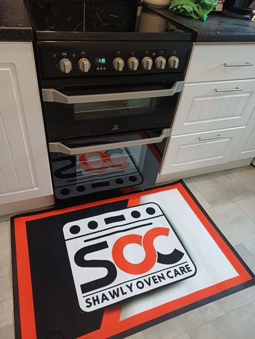 A kitchen oven with a colorful Shawly Oven Care mat in front of it.