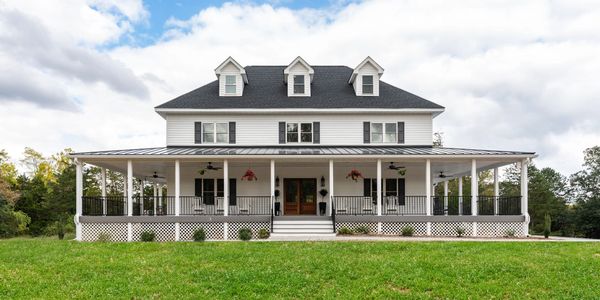 Large white house with a spacious wrap-around porch and green lawn.
