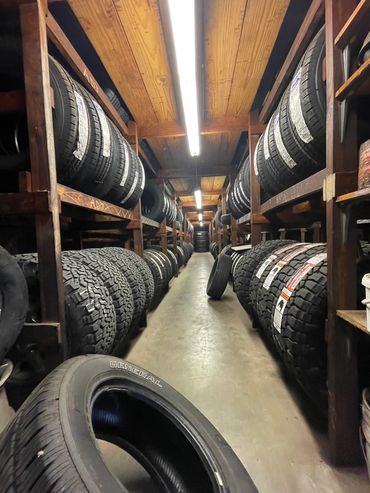A warehouse aisle filled with stacked tires on wooden shelves and a few tires on the floor.
