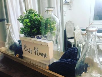 Centerpiece with famrhouse sign that reads Our Home, spools of navy blue yarn & glass bottles