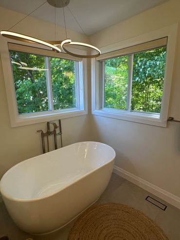 Modern bathroom with a white freestanding tub and large windows overlooking greenery.