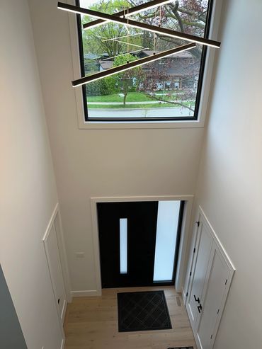 Modern entryway with a black door, large window, and sleek hanging lights.