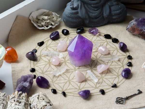 A purple crystal point surrounded by various crystals, sage, and a grey Buddha statue