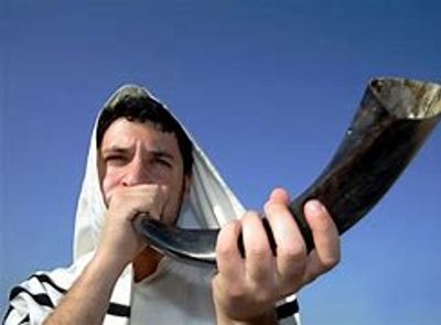 Man blowing a shofar outdoors against a blue sky.