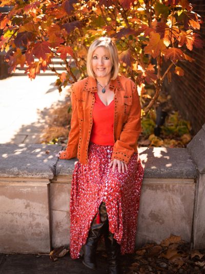 Woman in autumn outfit sitting on stone ledge under fall foliage.
