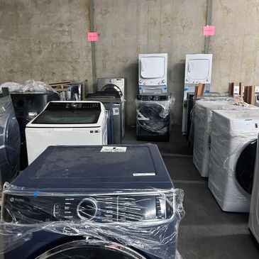 New washing machines and dryers wrapped in plastic in a warehouse.