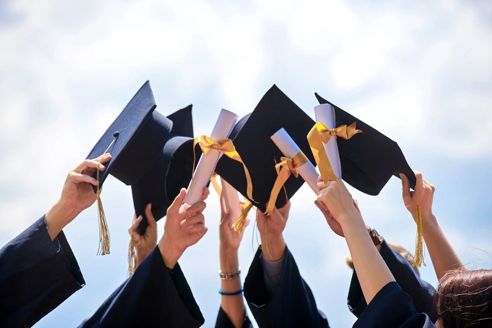 Graduates raising caps and diplomas in celebration against the sky.