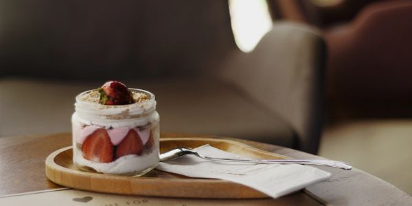 A jar dessert with strawberries and cream on a wooden tray.