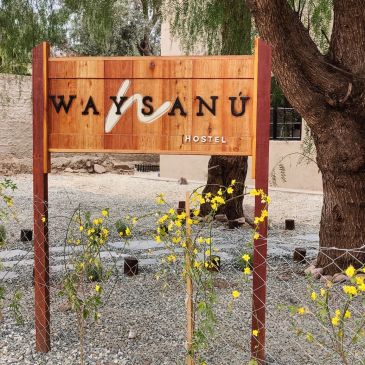 Wooden sign for Waysanú Hostel outdoors.