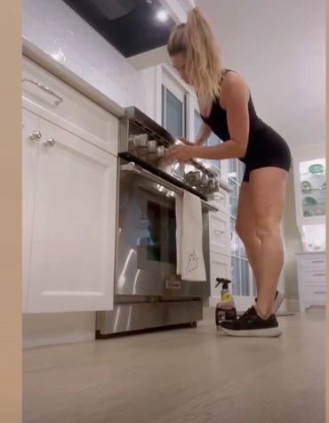 Woman in black outfit cleaning kitchen oven in modern home.