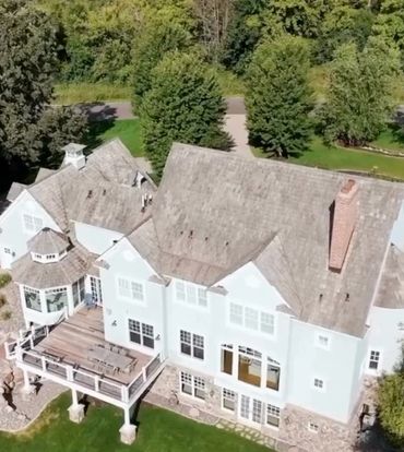 Large white two-story house with wooden deck and lush greenery.