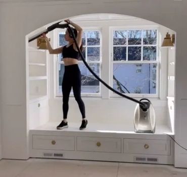 Woman using a vacuum cleaner on a windowsill seating area.