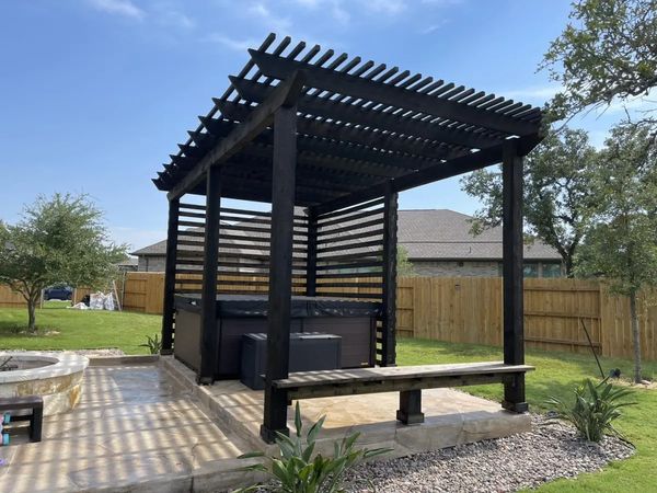 Backyard pergola with hot tub and stone flooring.