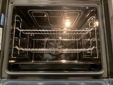Clean, empty oven interior with metal racks and a light on inside.