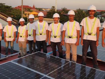 Technicians installing solar panels wearing helmets and safety harnesses.