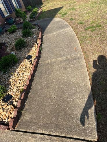 Curved concrete sidewalk beside a landscaped garden with solar lights.