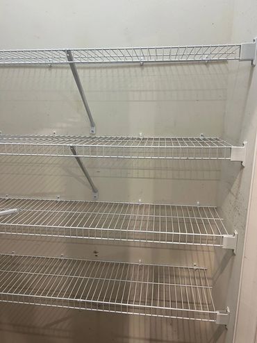 Empty white wire shelving units mounted on a wall.