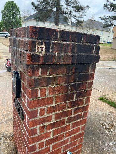 Brick mailbox stained with dark marks at the top in a suburban neighborhood.