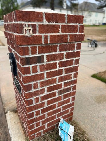 Red brick mailbox pillar with a torn blue flyer on the ground.