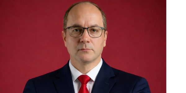 Confident man in a navy suit and red tie against a red background.