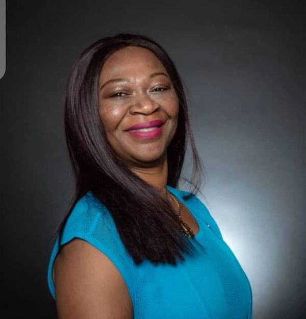 Smiling woman in a blue top poses against a dark background.