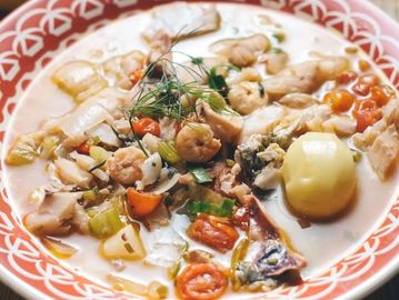 A bowl of seafood chowder with shrimp, vegetables, and a potato.