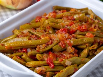 Green beans cooked with tomatoes and onions in a white dish.