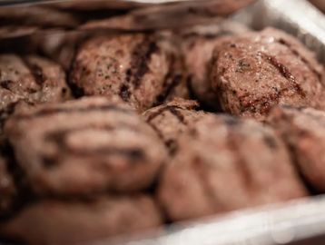 Grilled meat patties with visible grill marks in a tray.