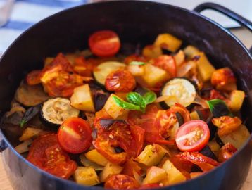 A pan of cooked ratatouille with tomatoes, zucchini, and herbs.