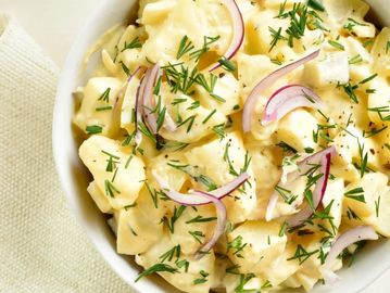 Creamy potato salad garnished with fresh dill and red onion slices in a white bowl.