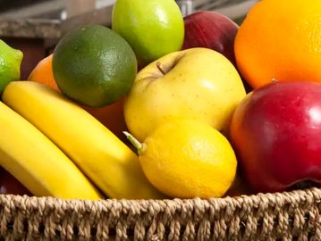 A basket filled with various fresh fruits including bananas, apples, lemons, and oranges.