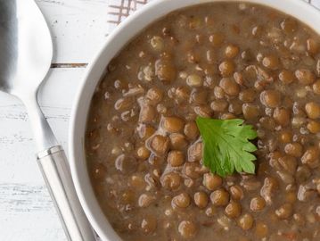 Bowl of lentil soup garnished with a fresh parsley leaf.