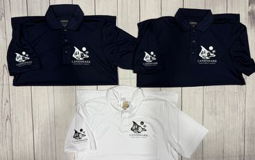 Three polo shirts with Landshark Investment Group logo, two navy and one white, laid on wooden floor.
