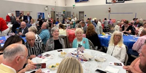 Seniors gathered around tables in a community hall for a social event.