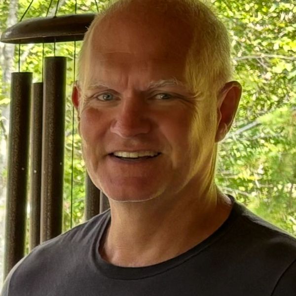 Smiling middle-aged man with short hair in front of wind chimes.