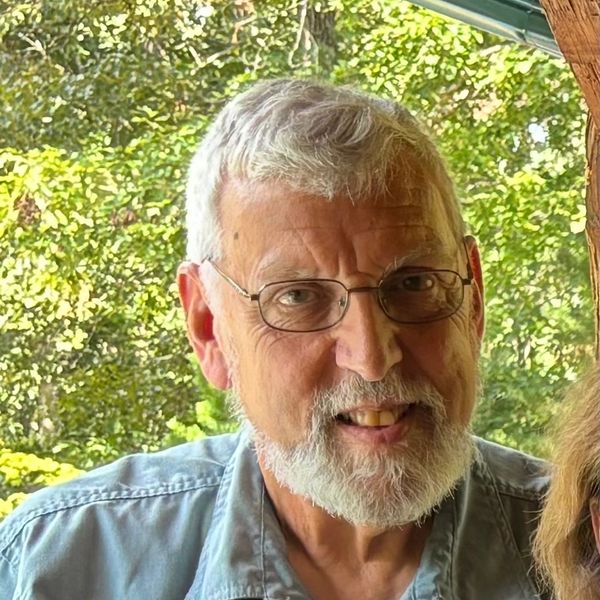 Smiling elderly man with glasses and white beard outdoors.